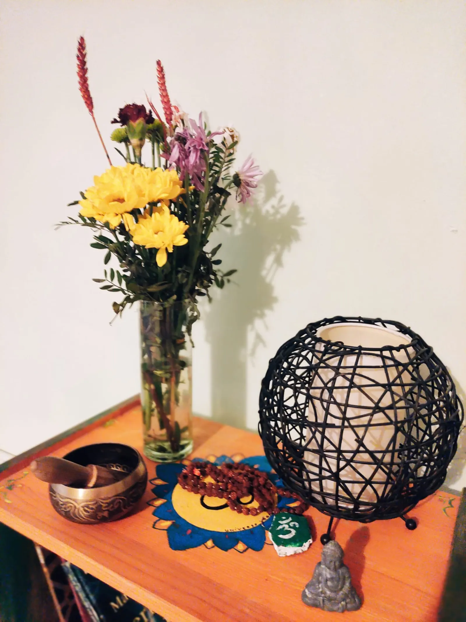 Rincón con flores amarillas, un cuenco tibetano y una lámpara de mimbre sobre un mueble naranja