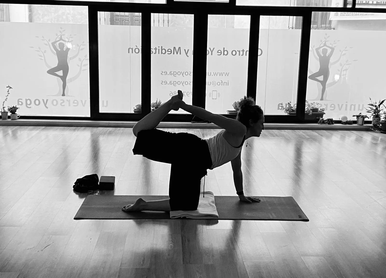Alumna en una postura de equilibrio sobre la esterilla, frente al ventanal, en blanco y negro