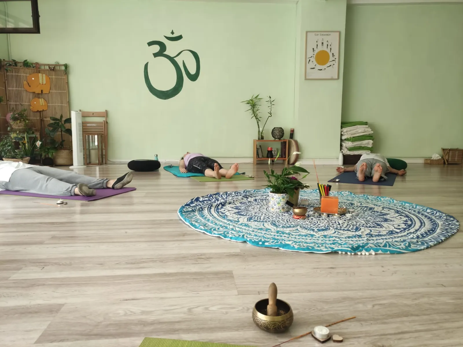 Alumnos tumbados alrededor de un mandala en el suelo, con un cuenco tibetano en primer plano